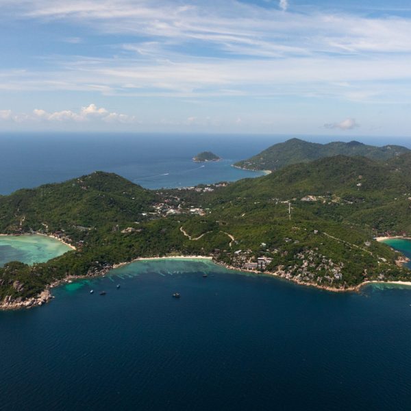 A wide-angle view of a tropical coastline featuring lush green hills and turquoise sea. Koh Tao, Thailand.